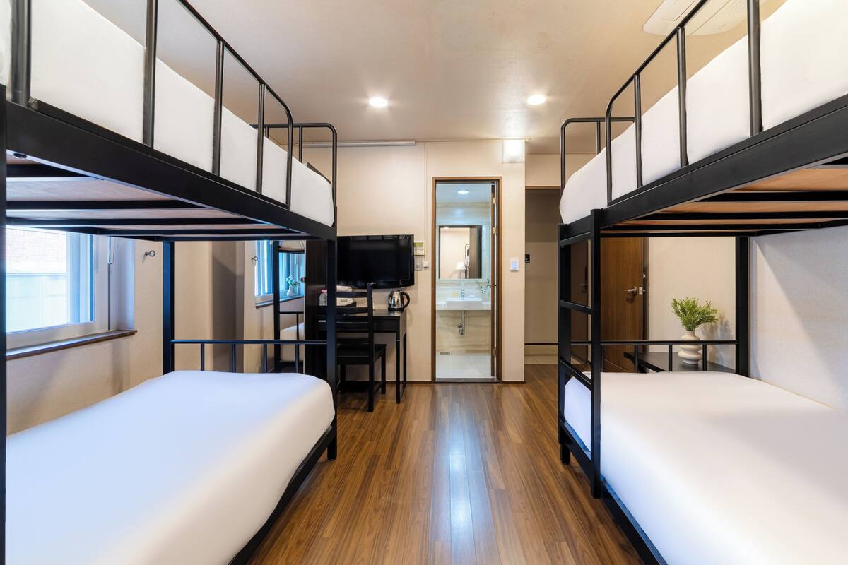 Un dormitorio con literas, un escritorio, un televisor y la puerta de un baño.