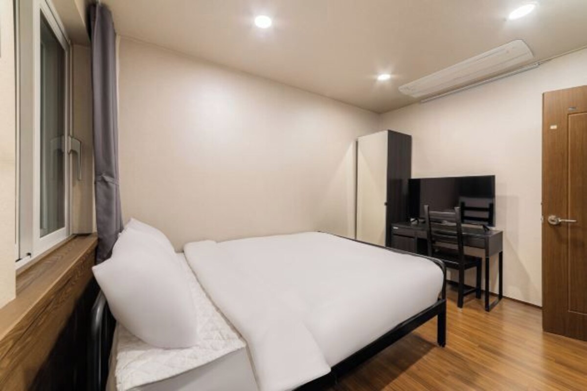 A bedroom with a bed, a desk, a chair, a wardrobe, and a door.