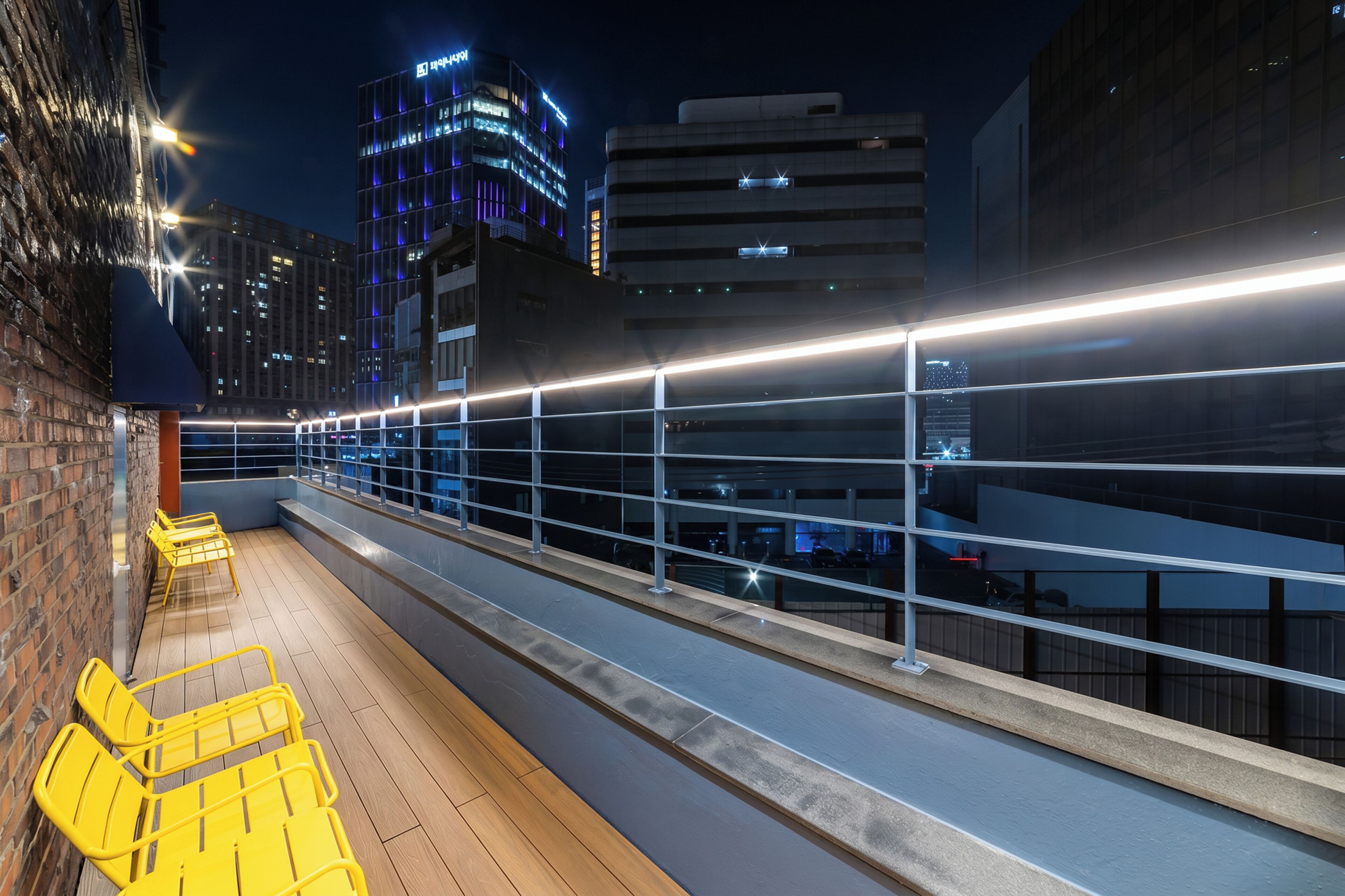 A rooftop terrace with yellow chairs, a railing, and city buildings in the background.