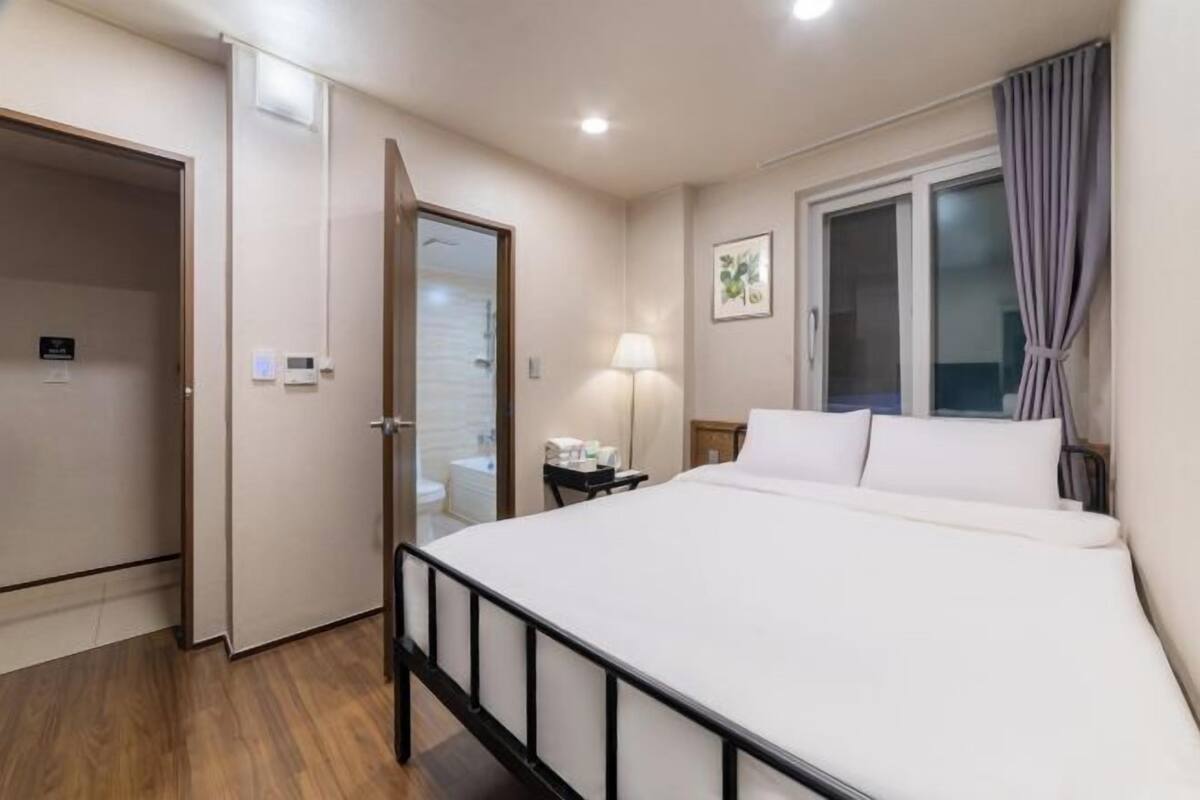 Une chambre d’hôtel avec un lit, une table de chevet, une lampe, une fenêtre avec des rideaux et une porte.
