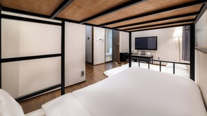 A modern hotel room with a large bed, a flat-screen TV, a desk with a lamp, and a sliding door leading to a bathroom.
