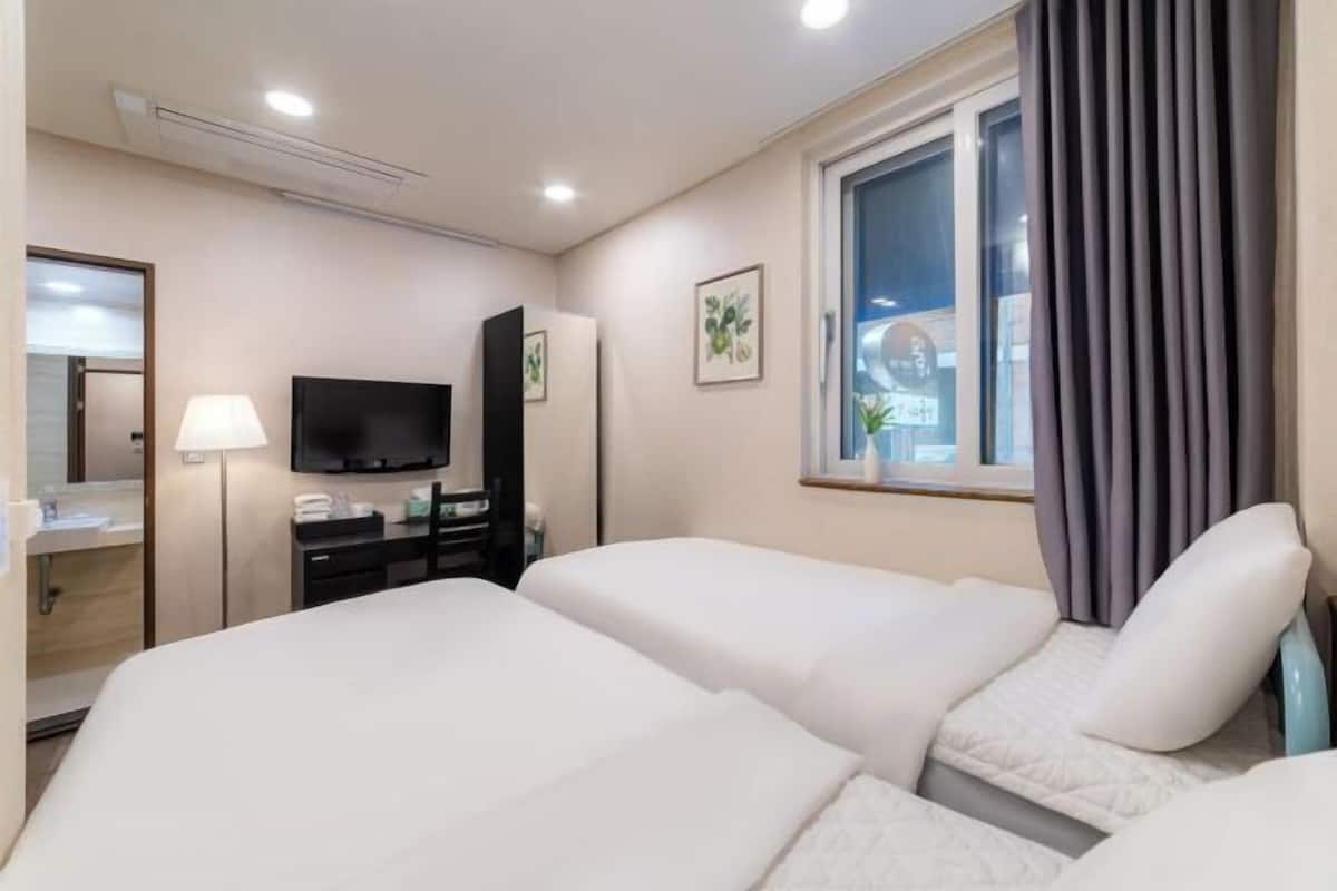 Une chambre d’hôtel avec deux lits, une télévision, un bureau avec une lampe et une fenêtre avec des rideaux.