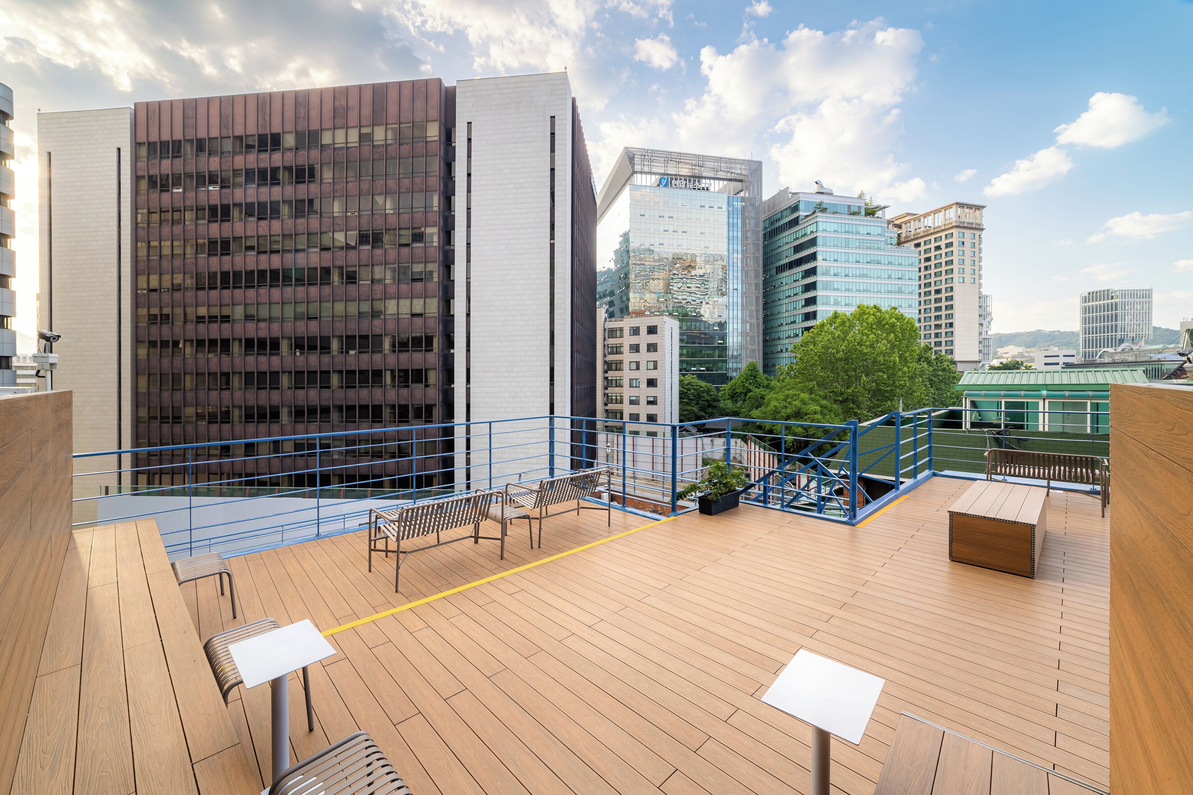 Una terraza en la azotea con piso de madera, barandas metálicas y zonas de estar.
