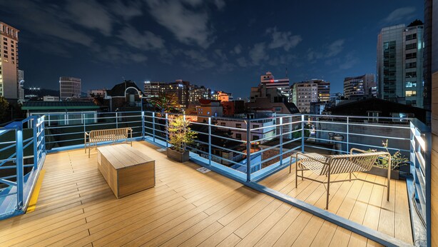A rooftop terrace with wooden flooring, metal railings, and seating areas.