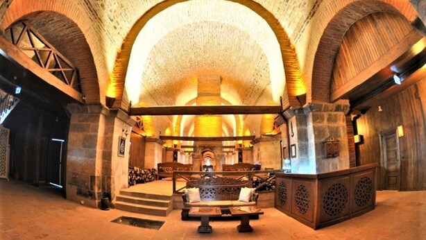 Een ruime lobby met een hoge gewelfde plafond, stenen muren en een centraal zitgedeelte.