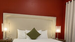 Un lit bien fait, avec du linge de lit blanc et un coussin vert en guise d’élément décoratif, flanqué de deux tables de chevet sur lesquelles sont posées des lampes.