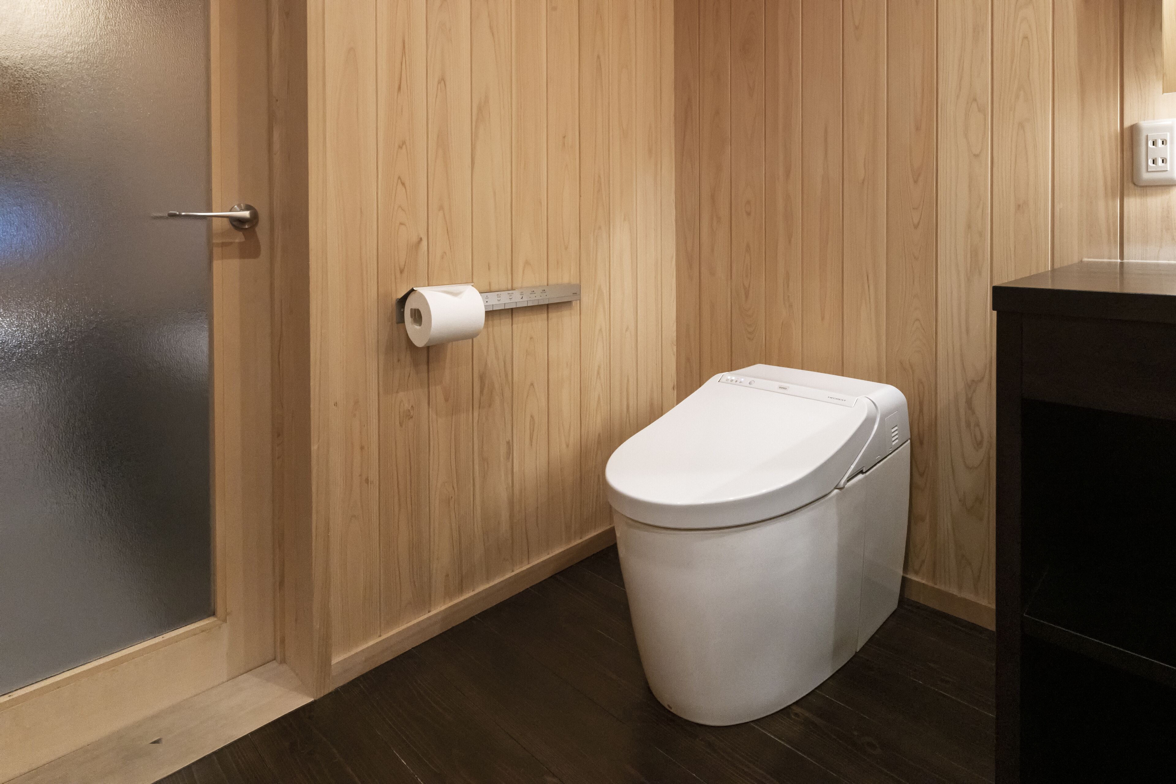 A compact bathroom with a wooden wall, a white toilet, and a roll of toilet paper.