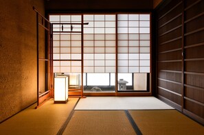 Una habitación japonesa tradicional con suelo de tatami, puertas correderas shoji y vistas a un paisaje urbano.
