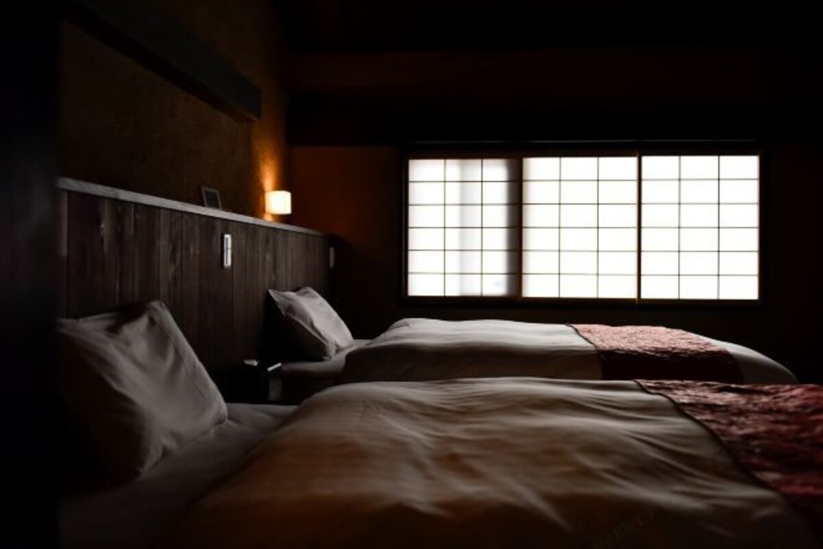 A dimly lit room with two beds, a wooden headboard, and a window with a grid pattern.