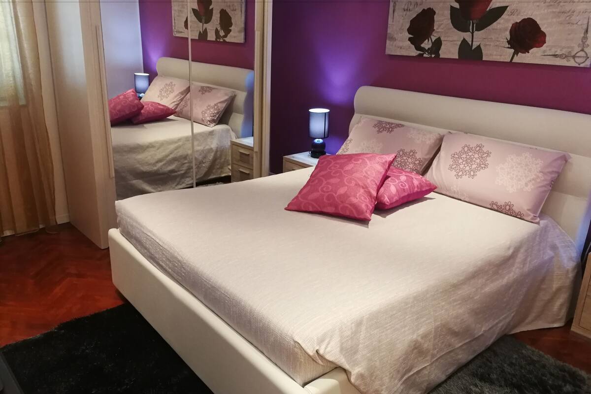 A bedroom with a bed, two nightstands, a mirror, and decorative pillows.