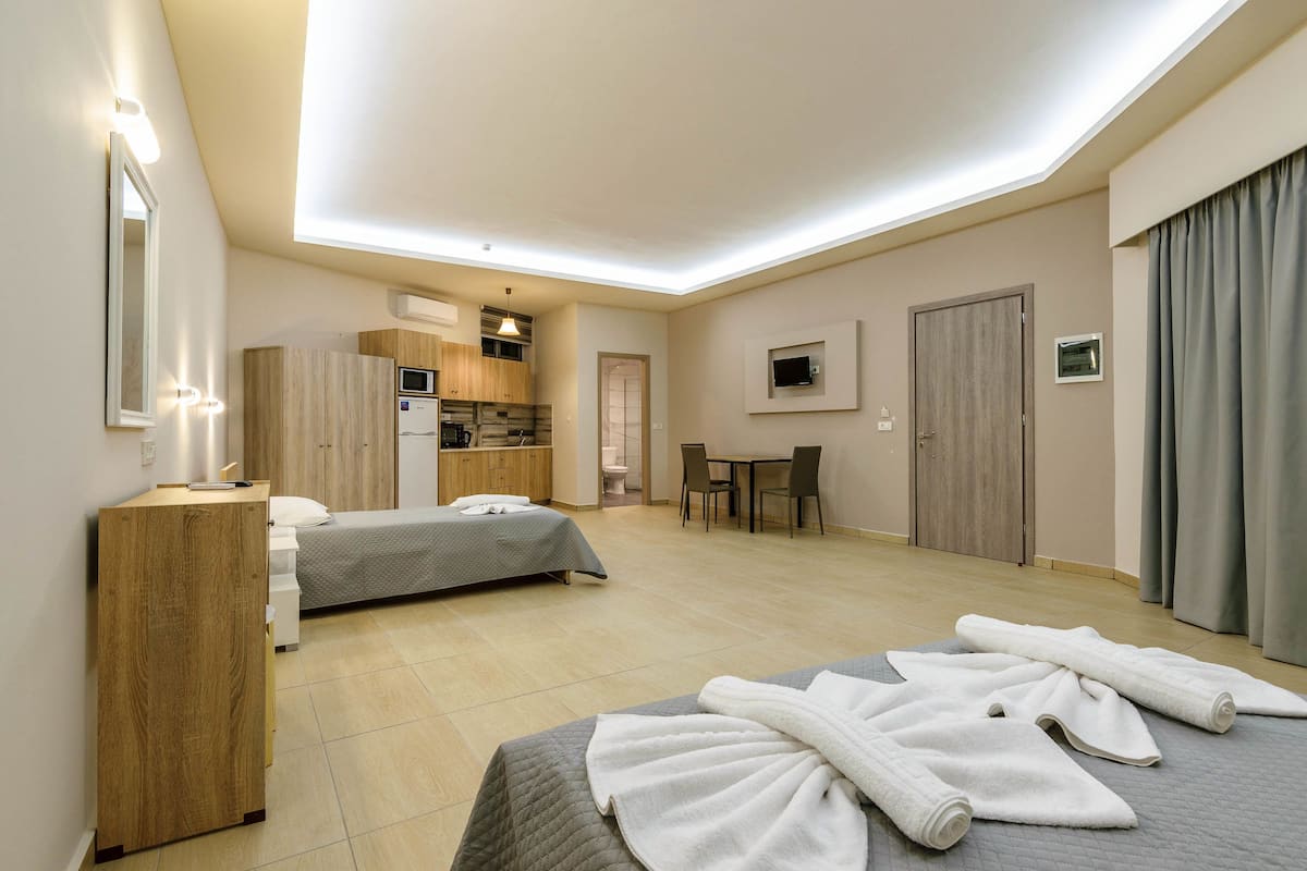 A hotel room with two beds, a kitchenette, a dining area, and a bathroom.