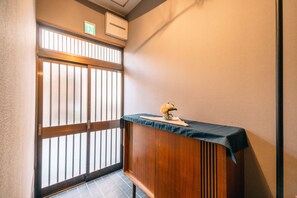 A small, enclosed space with a wooden counter, a small table with a vase, and a sliding door with vertical bars.