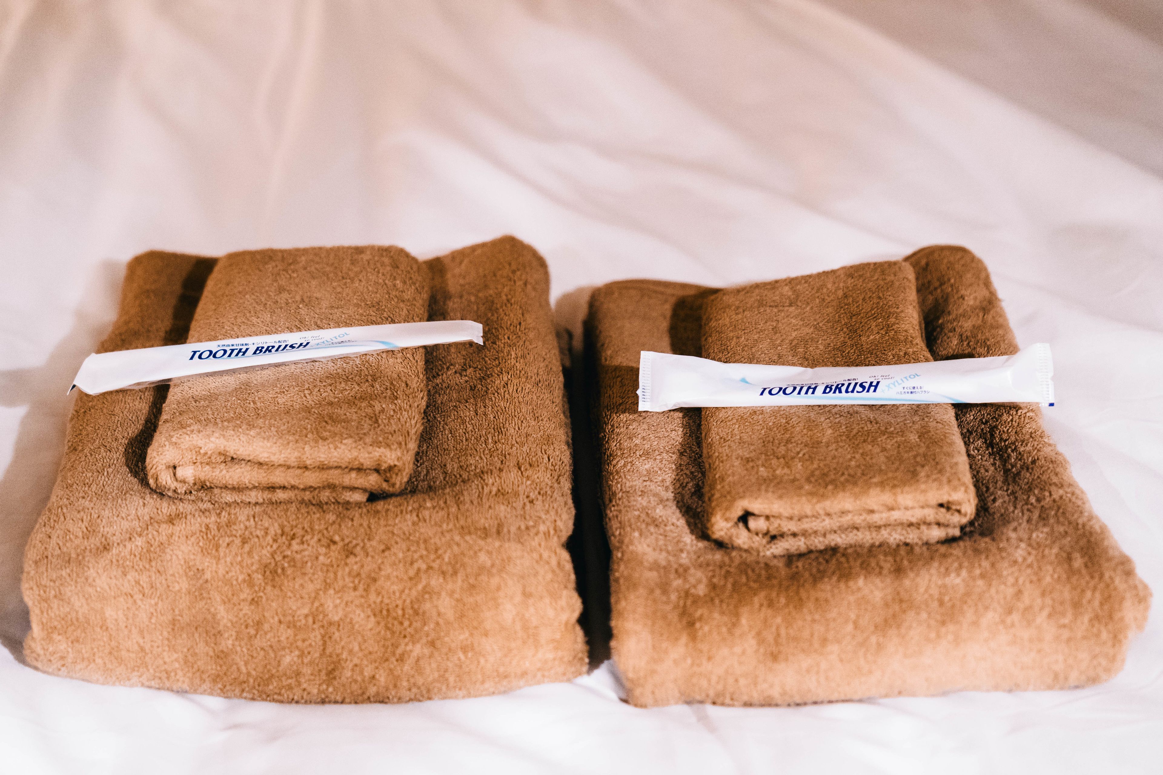 Dos toallas marrones ordenadamente dobladas sobre una cama, con un cepillo de dientes y pasta dental.