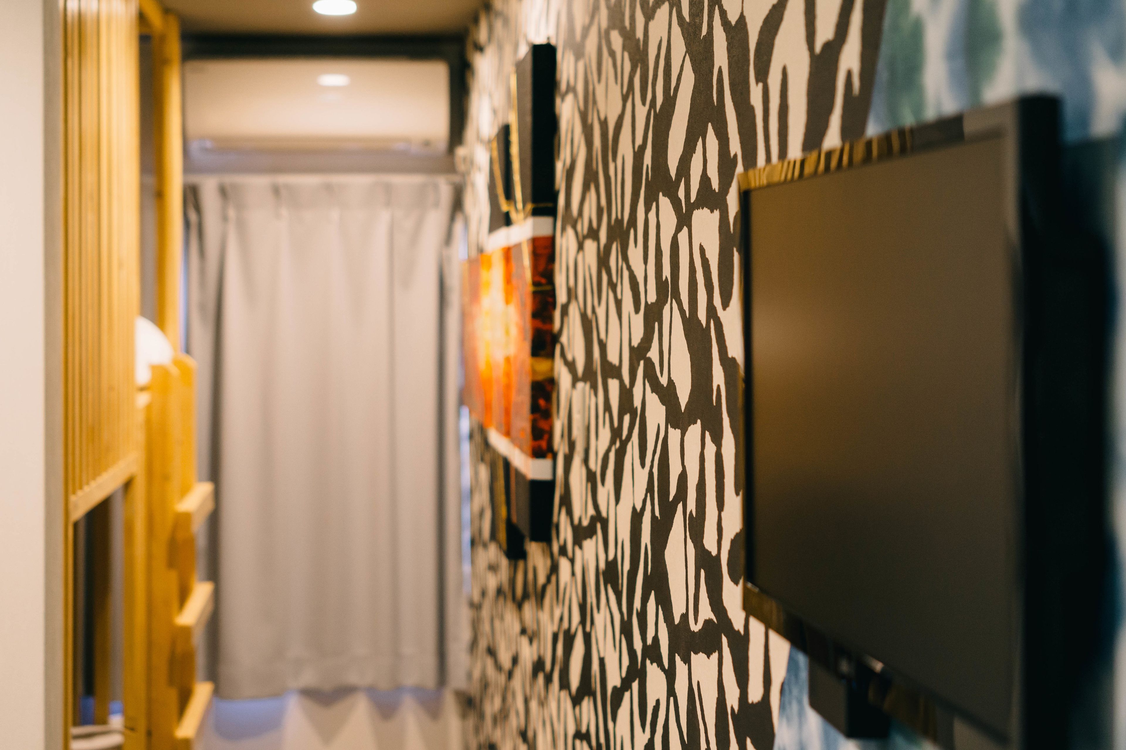 A room with a television mounted on the wall, a patterned wallpaper, and a wooden structure on the left.