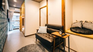 A modern hotel room with a sofa, a small table with a clock, and a window with a view. - IKIDANE HOUSE OSAKA Kyobashi (Osaka)