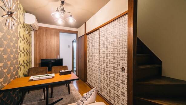 A modern interior with a dining area, a sofa, a staircase, and a decorative wall. - IKIDANE HOUSE OSAKA Kyobashi (Osaka)