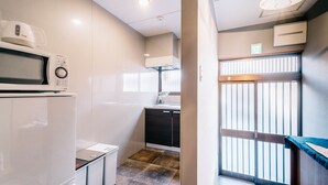 A compact kitchen with a microwave, a small refrigerator, and a dishwasher. There is a window with blinds and a view of the outside. - IKIDANE HOUSE OSAKA Kyobashi (Osaka)