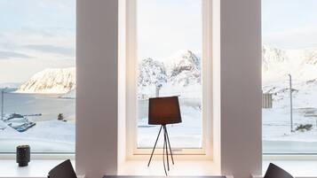 A modern meeting room with a large table and chairs, a floor lamp, and a view of snowy mountains and a body of water through large windows.