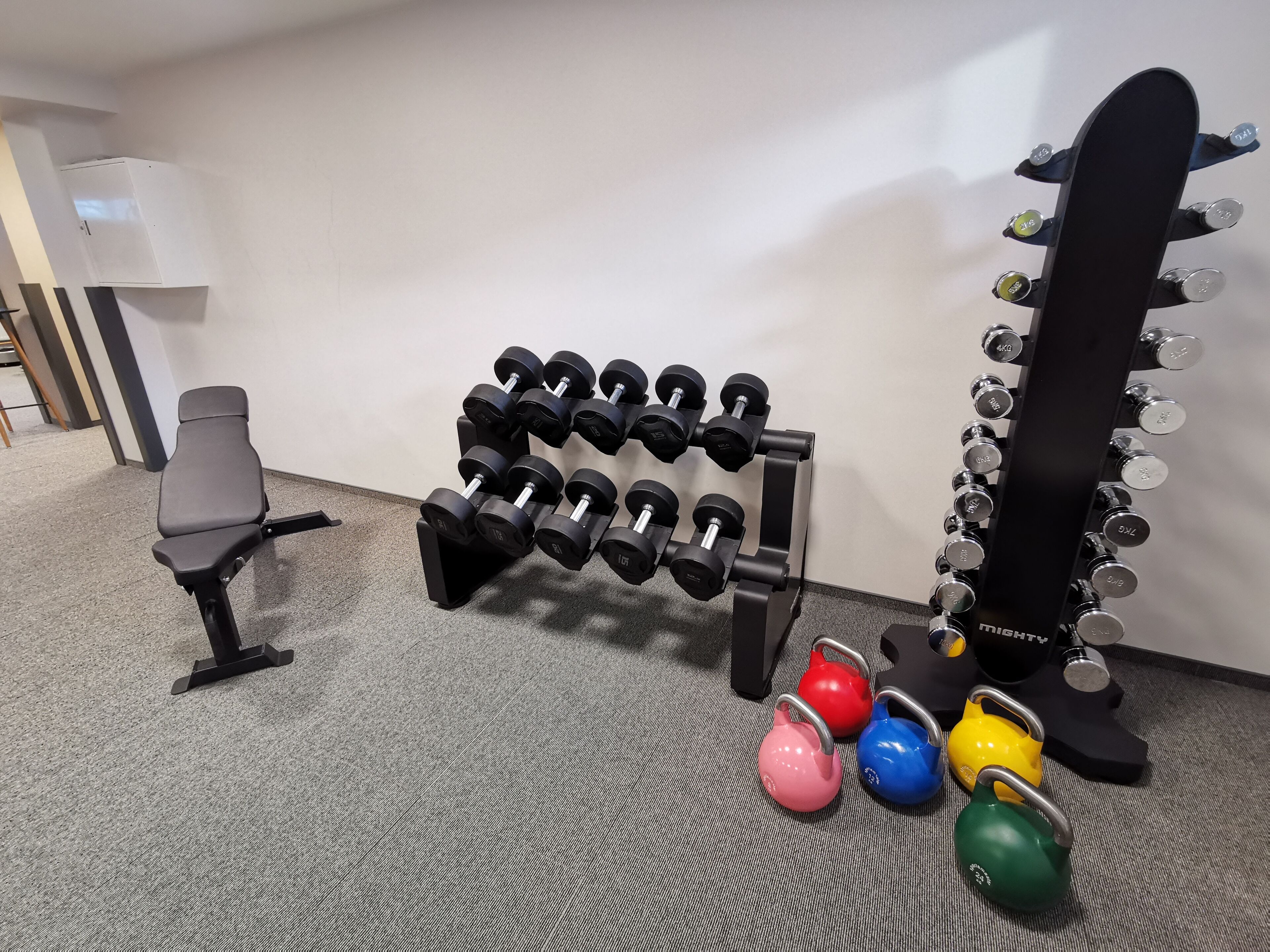 Een sportschool met een bank, een dumbbellrek, kettlebells en een squatrek.