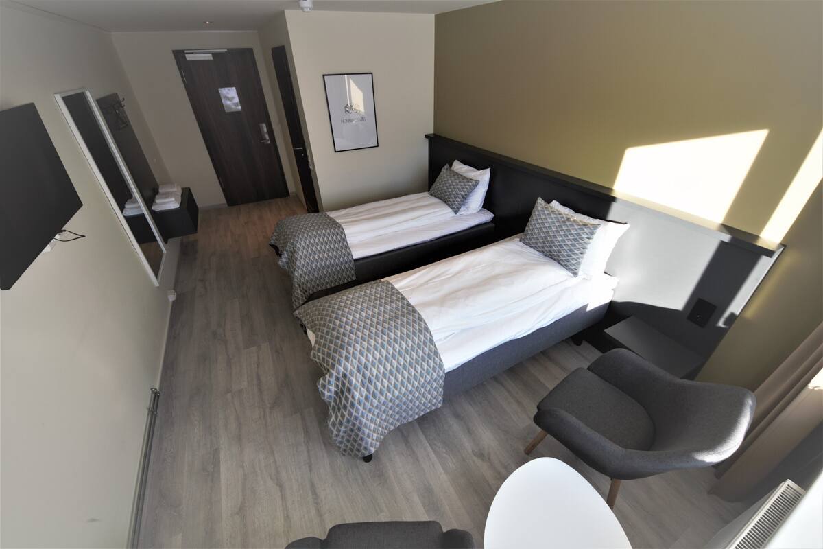 A hotel room with two beds, a desk, a chair, and a bathroom.