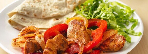 A plate of grilled chicken with bell peppers and onions, accompanied by flatbread and a side salad.