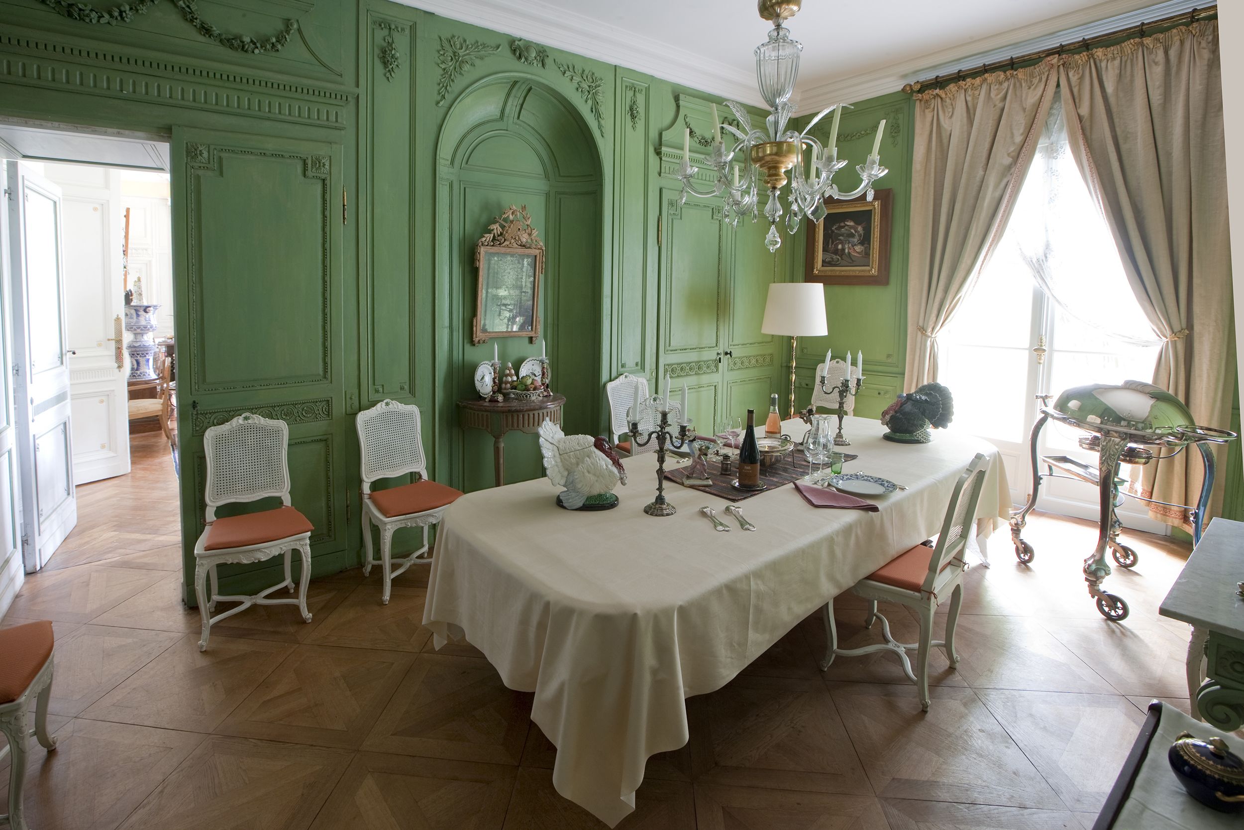 Una sala da pranzo con parete verde, sedie bianche, tavolo rotondo e lampadario.