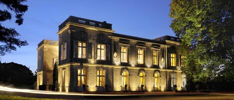 A large, historic building with multiple windows and a symmetrical facade, surrounded by a well-maintained lawn.