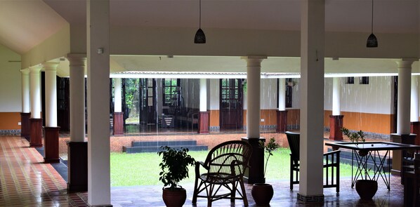 A covered outdoor area with columns, a tiled floor, and potted plants.