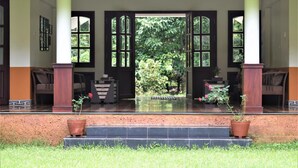 A covered entrance with a tiled floor, two potted plants, and a sign above the door. - 3 Hills County (Vythiri)