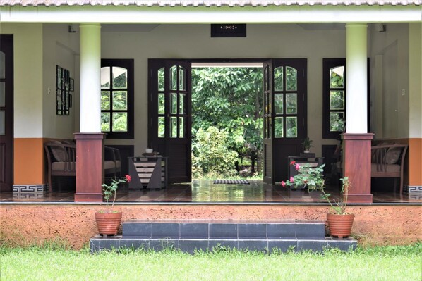 A covered entrance with a tiled floor, two potted plants, and a sign above the door. - 3 Hills County (Vythiri)