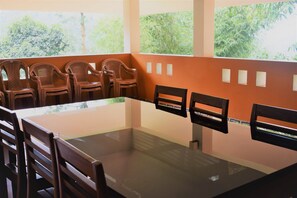 A conference room with a glass table, wooden chairs, and a view of greenery through large windows.
