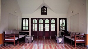 A room with a high ceiling, large windows, and a patterned floor. There are two sofas and a table in the center. - 3 Hills County (Vythiri)