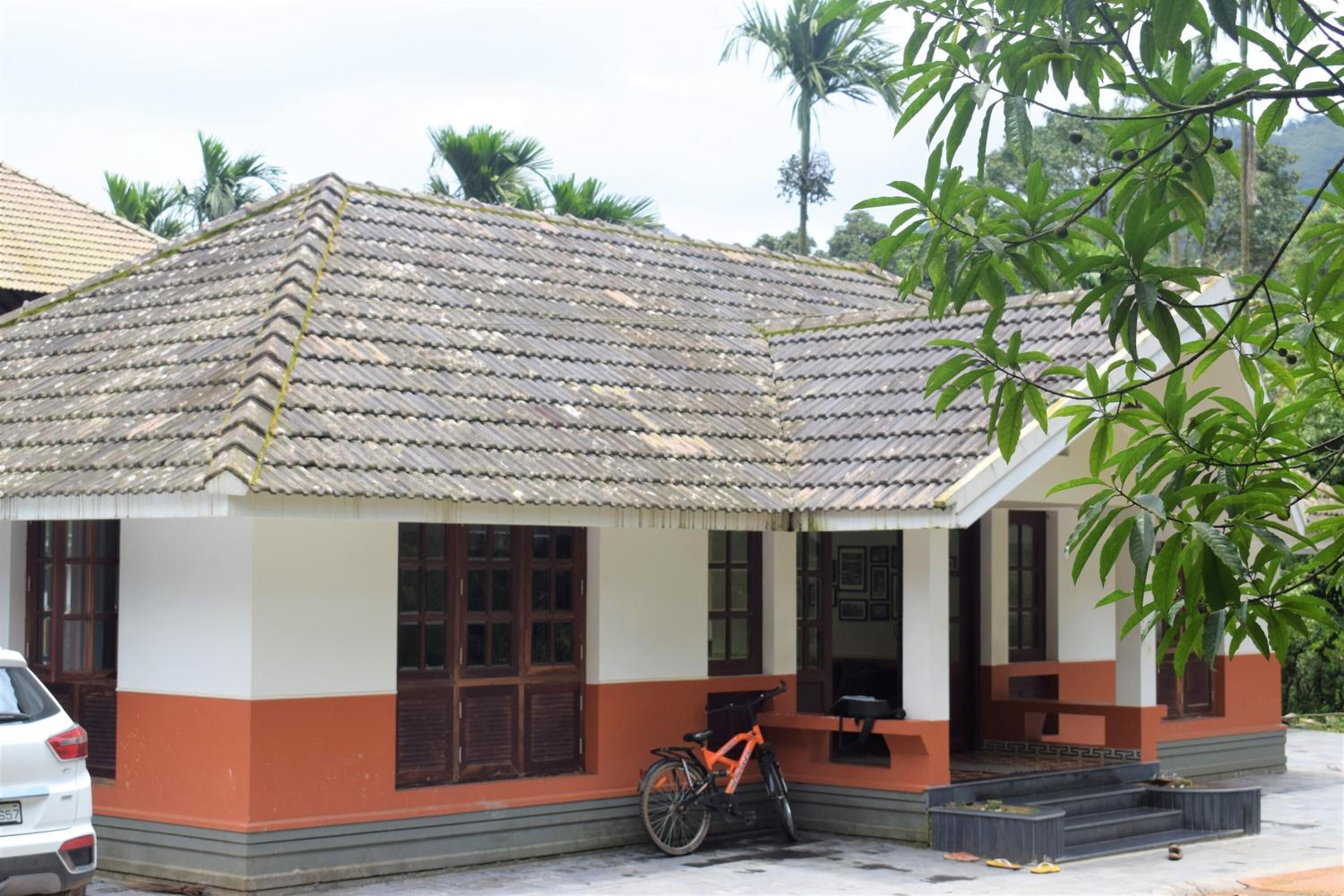 Uma casa térrea com telhado de cerâmica, uma bicicleta estacionada na frente e um pequeno alpendre.