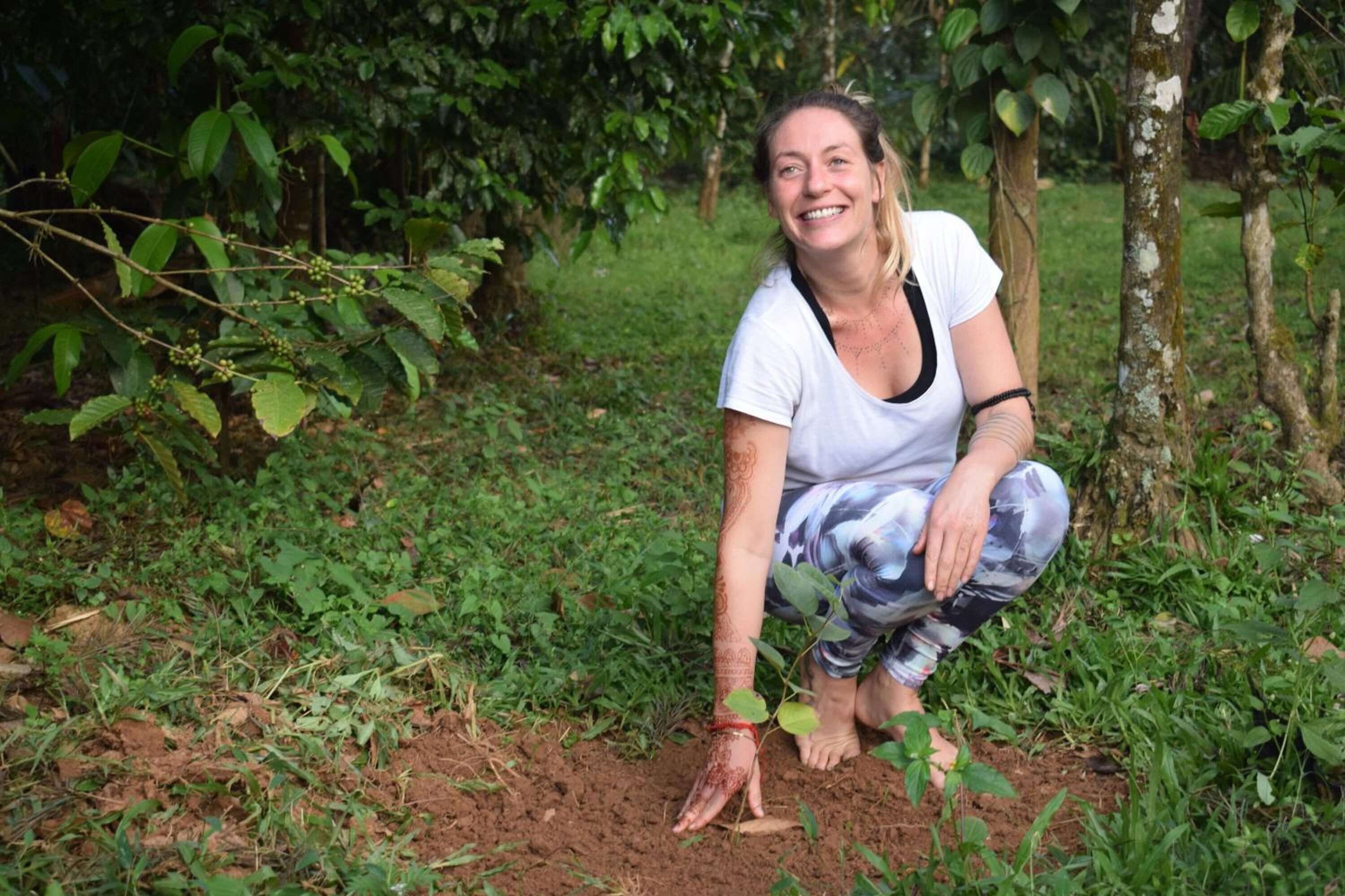 Una persona agachada en un jardín con follaje verde y árboles.