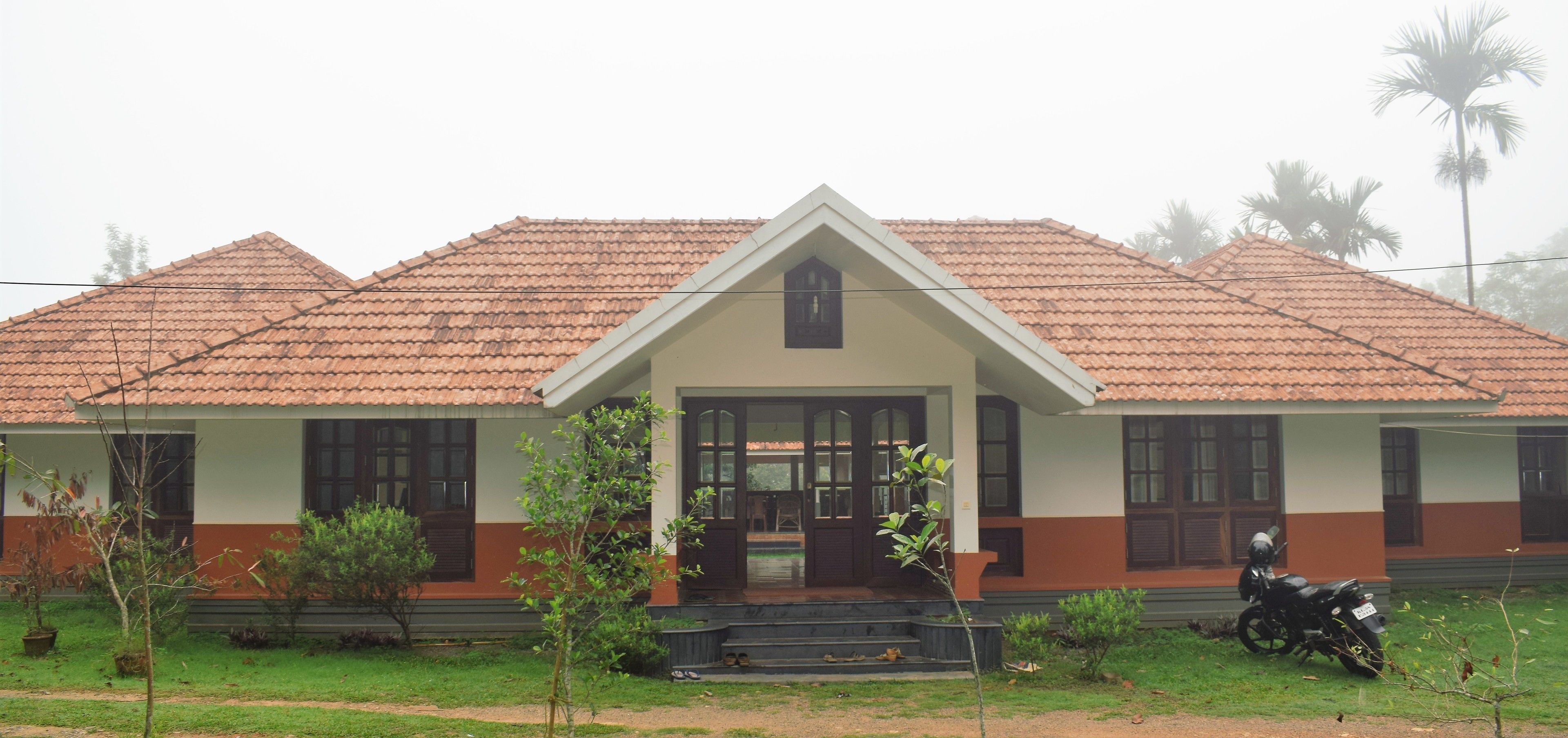 A two-story building with a tiled roof, a central entrance with a small porch, and a motorcycle parked in front.