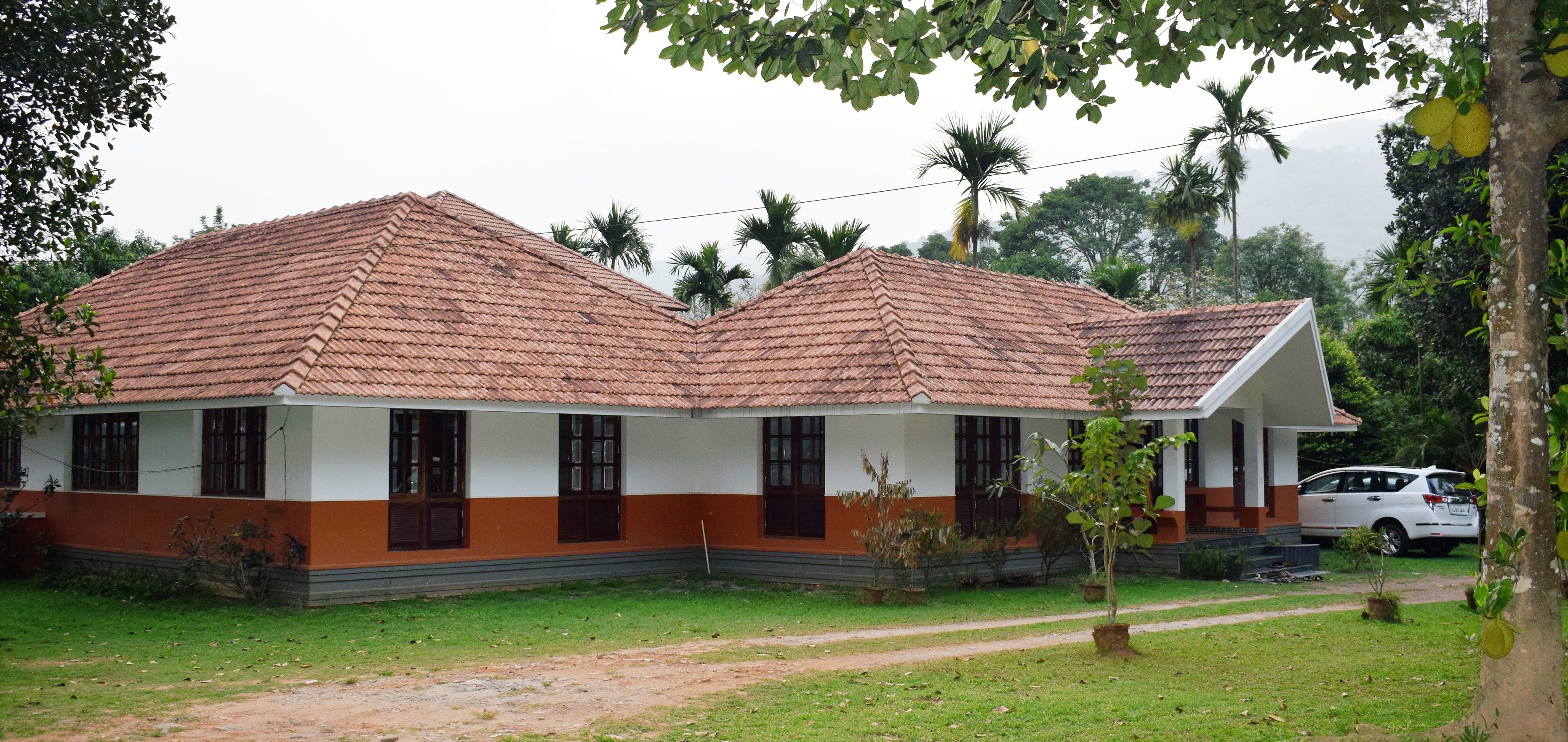 A two-story building with a tiled roof, surrounded by greenery and palm trees.