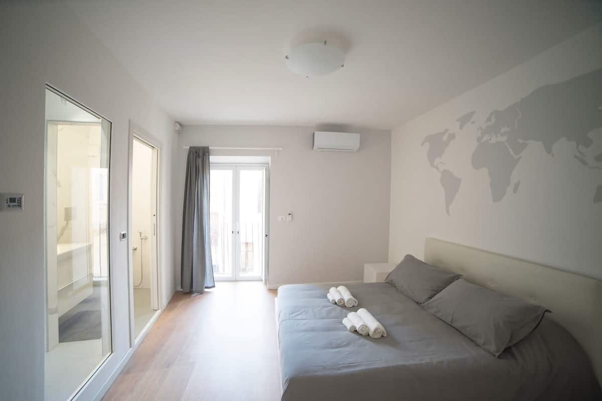 A modern bedroom with a large bed, a glass door leading to a balcony, and a world map on the wall.