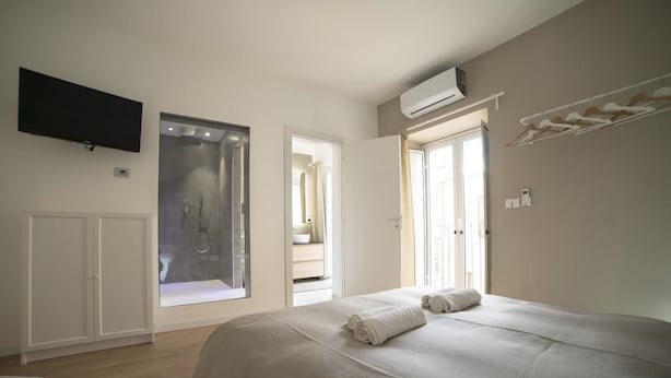 A bedroom with a large bed, a TV mounted on the wall, and a window overlooking a bathroom. - Suite Dreams (Agrigento)