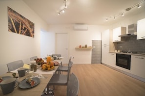 Una cocina moderna con comedor, que incluye estufa, horno y una mesa de comedor servida con platos, tazas y un frutero.