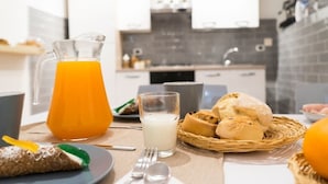 A breakfast table with a pitcher of orange juice, a glass of milk, and a basket of bread rolls. - Suite Dreams (Agrigento)
