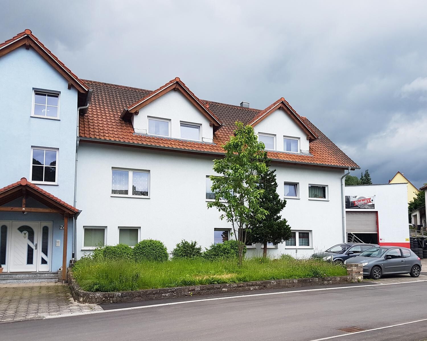 Un immeuble résidentiel à deux étages, avec un toit recouvert de tuiles rouges, de nombreuses fenêtres et un petit arbre devant.