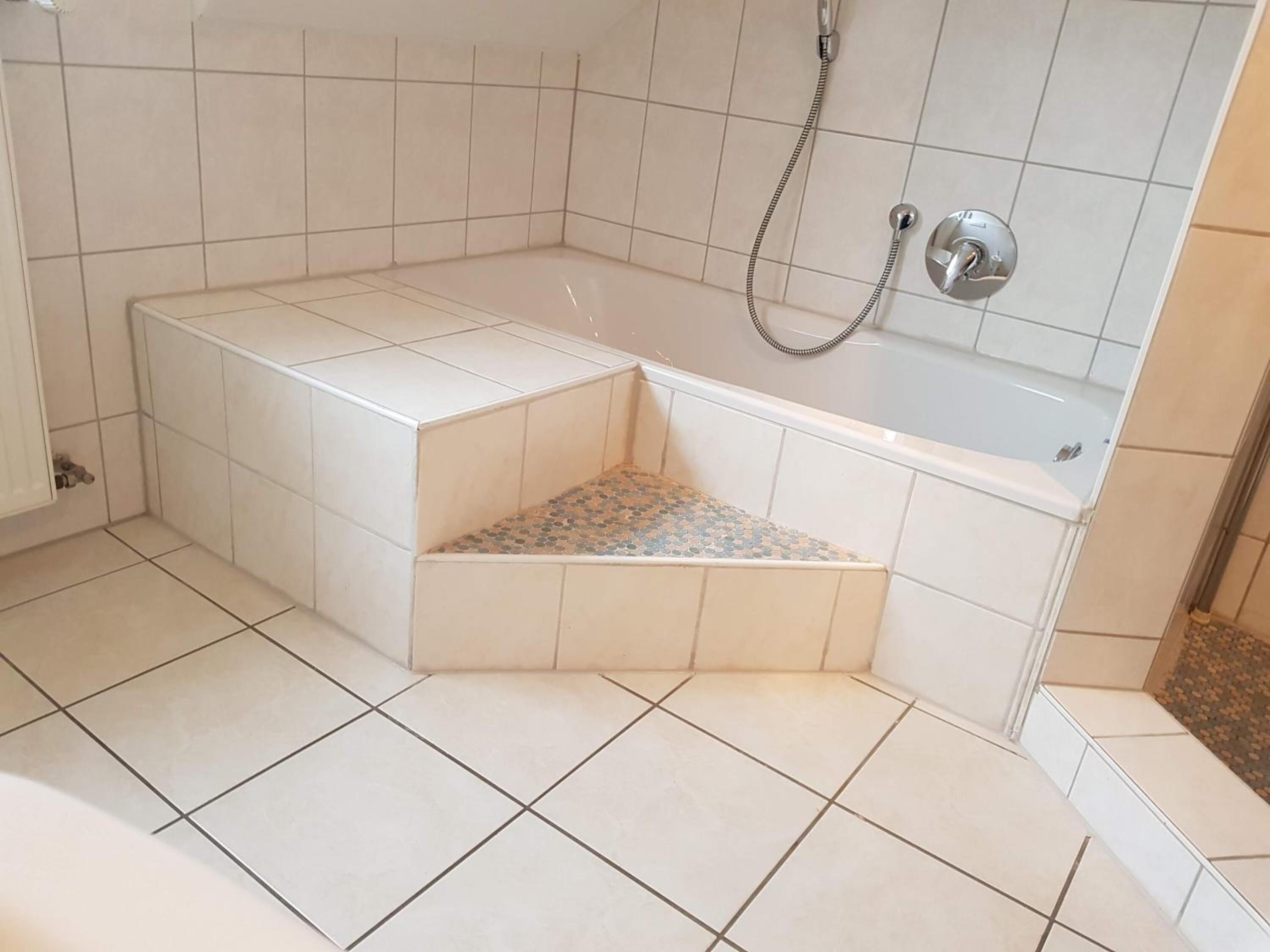 A bathroom with a bathtub, shower, and a small step leading to a tiled floor.