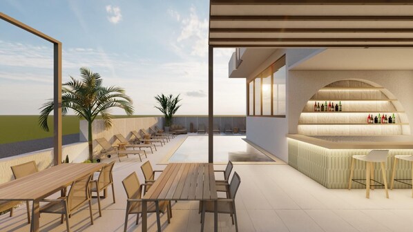 A rooftop terrace with a long wooden table and chairs, a bar area with a counter and stools, and palm trees in the background.
