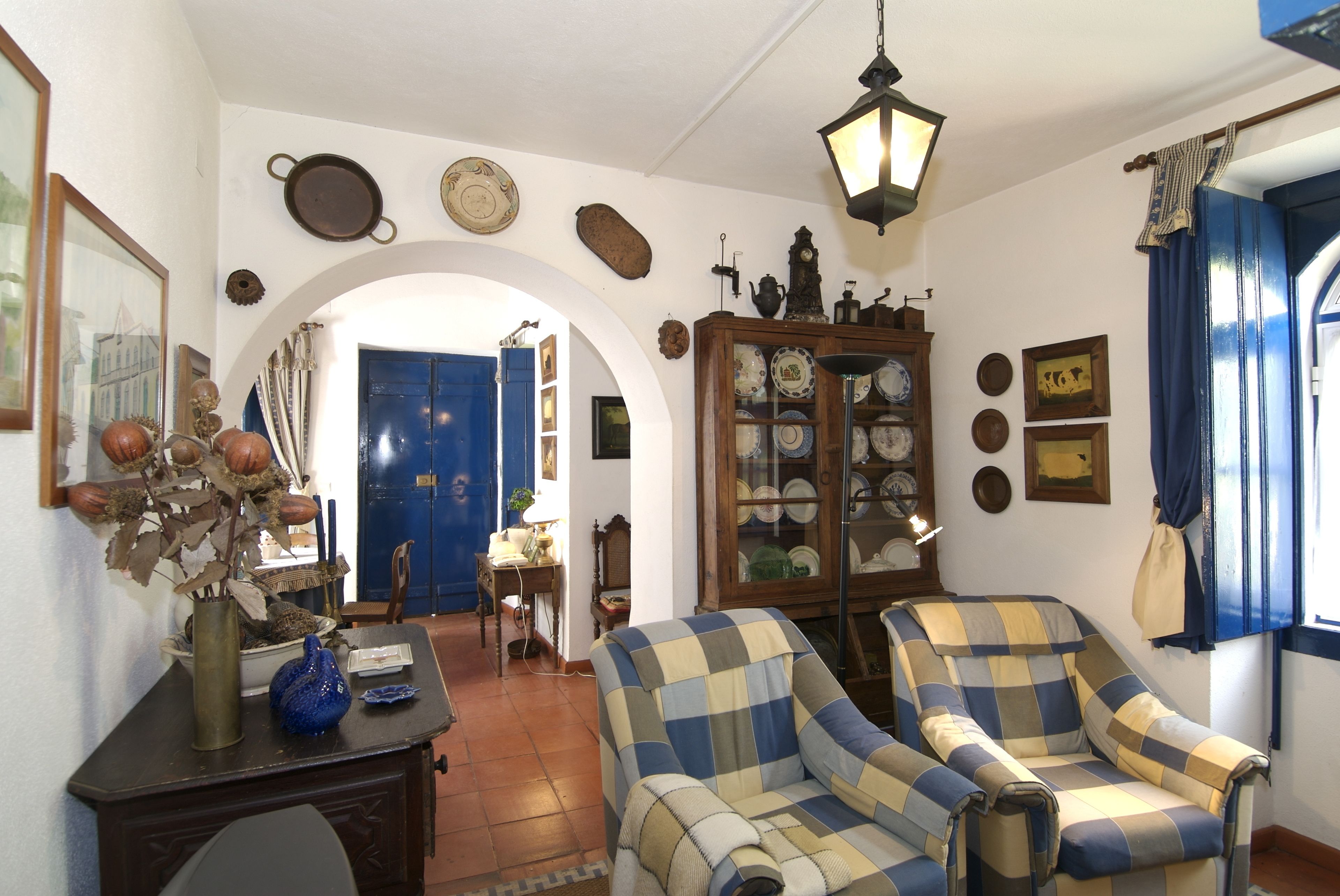 Een kamer met een geruite fauteuil, een houten kast met servies en een blauwe deur.