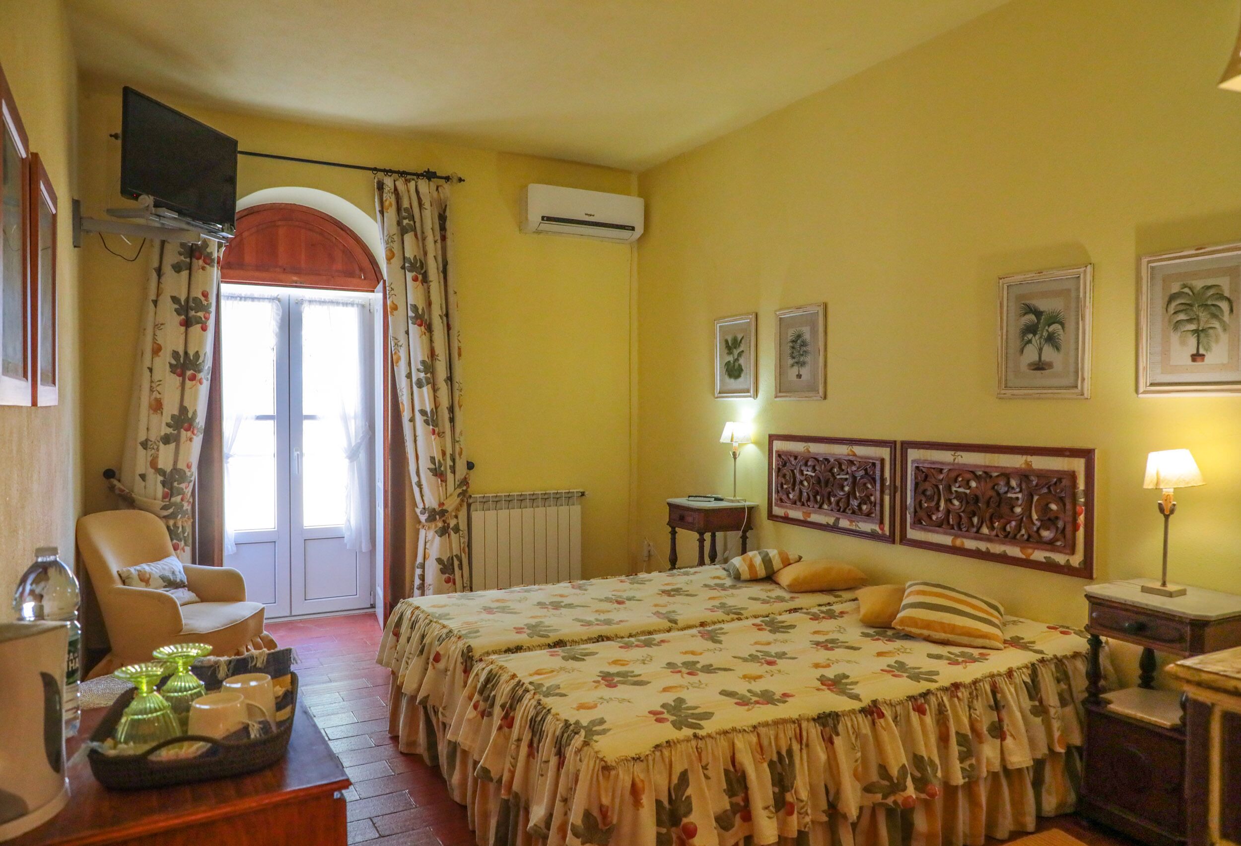 Una habitación de hotel con dos camas, una silla, una mesa con una bandeja de vasos y un televisor.