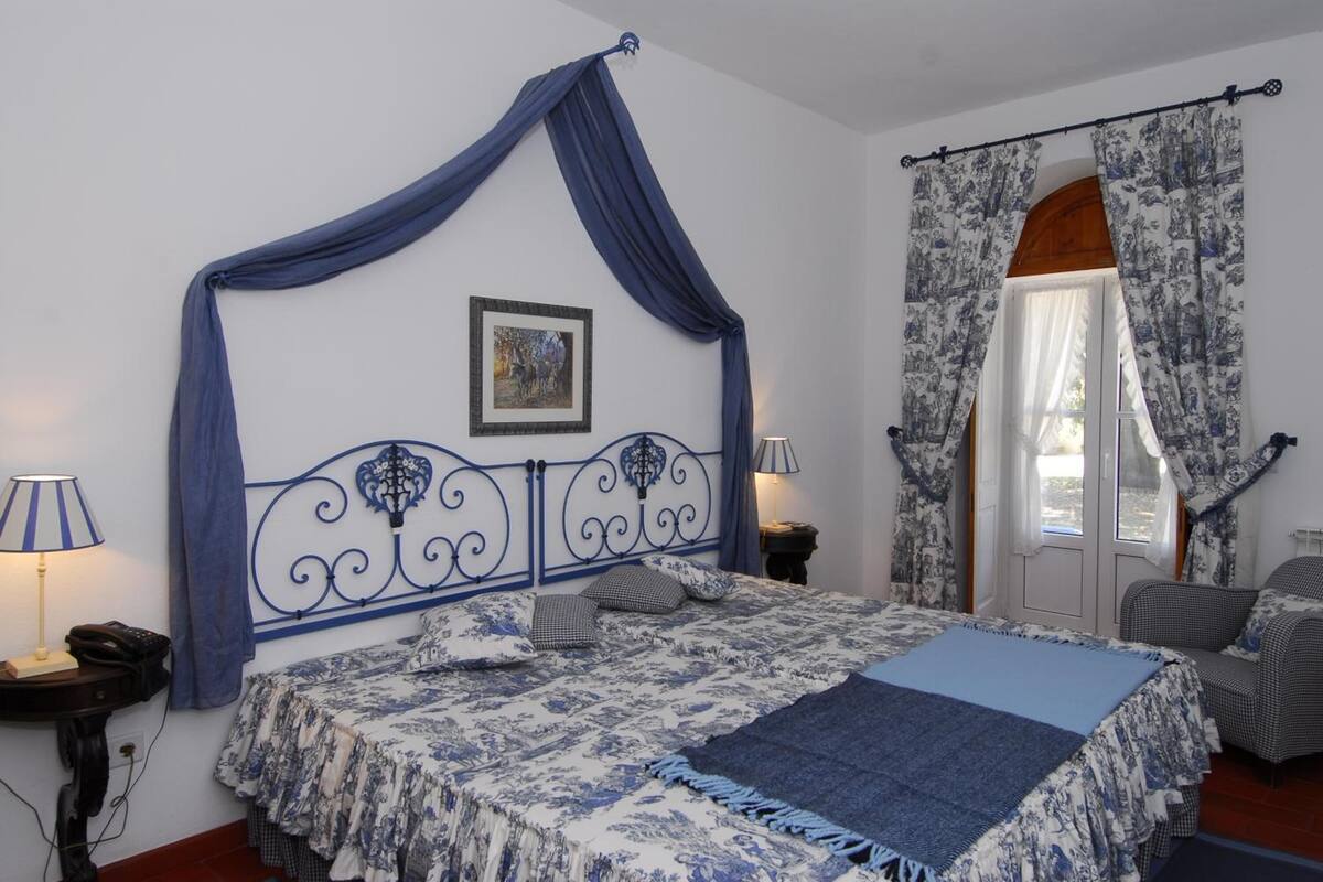 Ein Schlafzimmer mit Himmelbett, einem Bild an der Wand und einem Fenster mit Vorhängen.