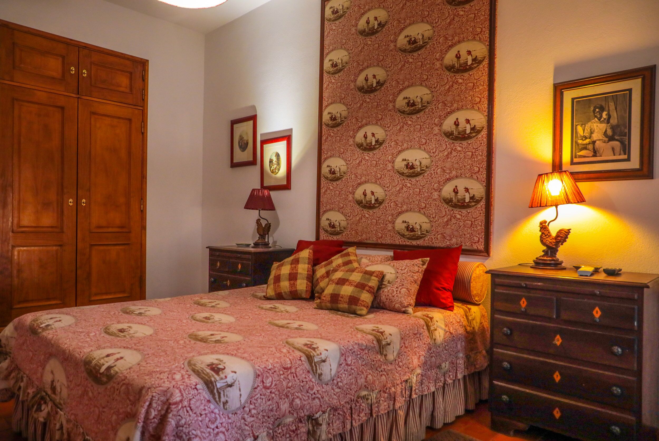 A bedroom with a large bed, wooden wardrobe, and a dresser with a lamp.