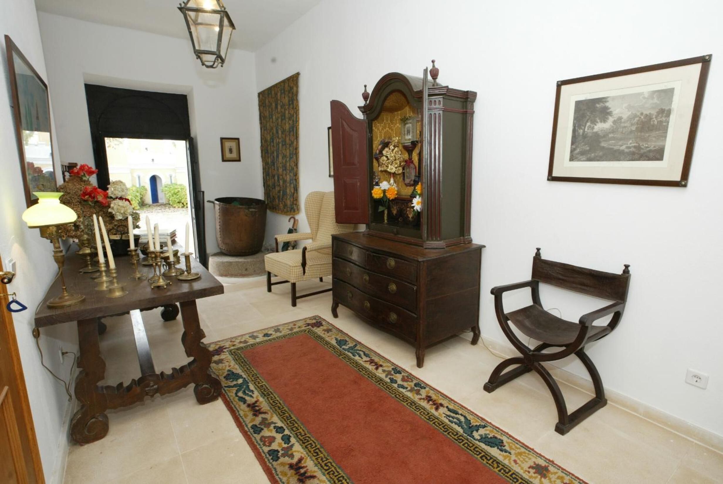 A traditional room with a wooden dresser, a chair, a table with candles, and a framed picture on the wall.