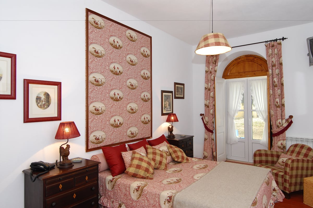 Ein Schlafzimmer mit einem Bett, zwei Nachttischen, einer Lampe, einer Kommode und einer Tür, die auf einen Balkon führt.