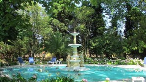 Une piscine agrémentée d’une fontaine à plusieurs niveaux, entourée d’une végétation luxuriante et de chaises longues.